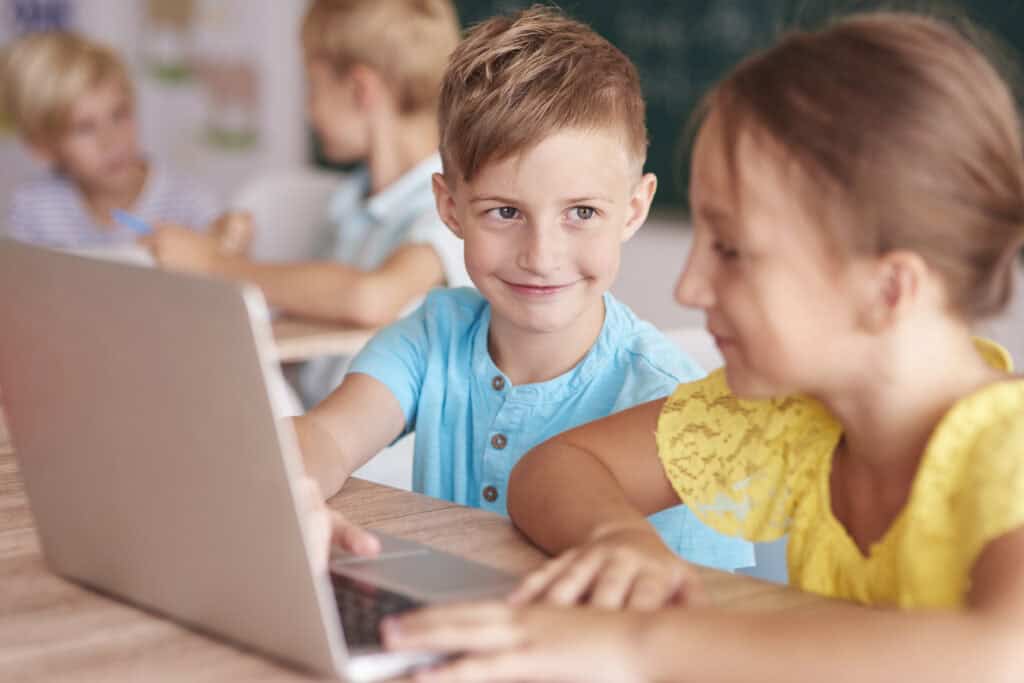 Zwei Kinder blicken in der Schule auf einen Laptop und haben Spaß.