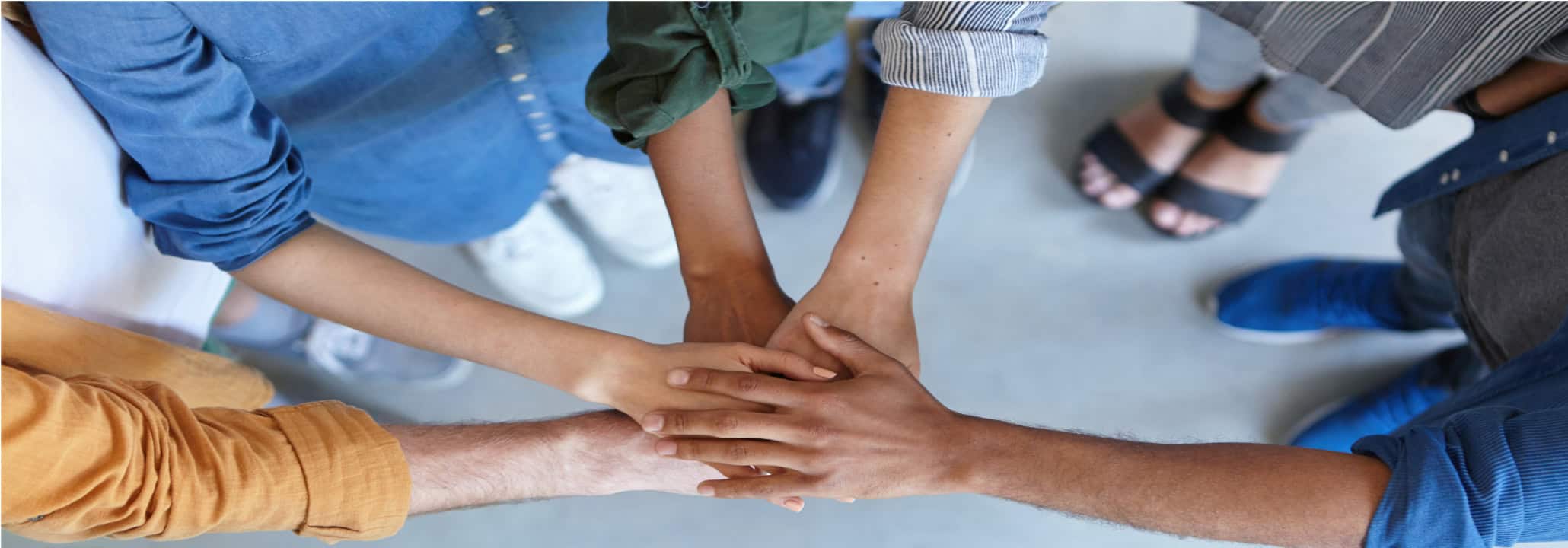 Eine Gruppe an Menschen stapelt die Hände aufeinander. Wir arbeiten im Team.