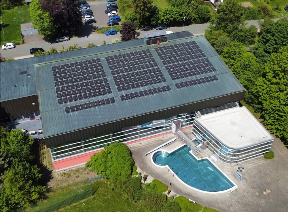 Das Gebäude Aquawell, von oben mit Photovoltaikanlagen und einem Schwimmbecken im Außenbereich