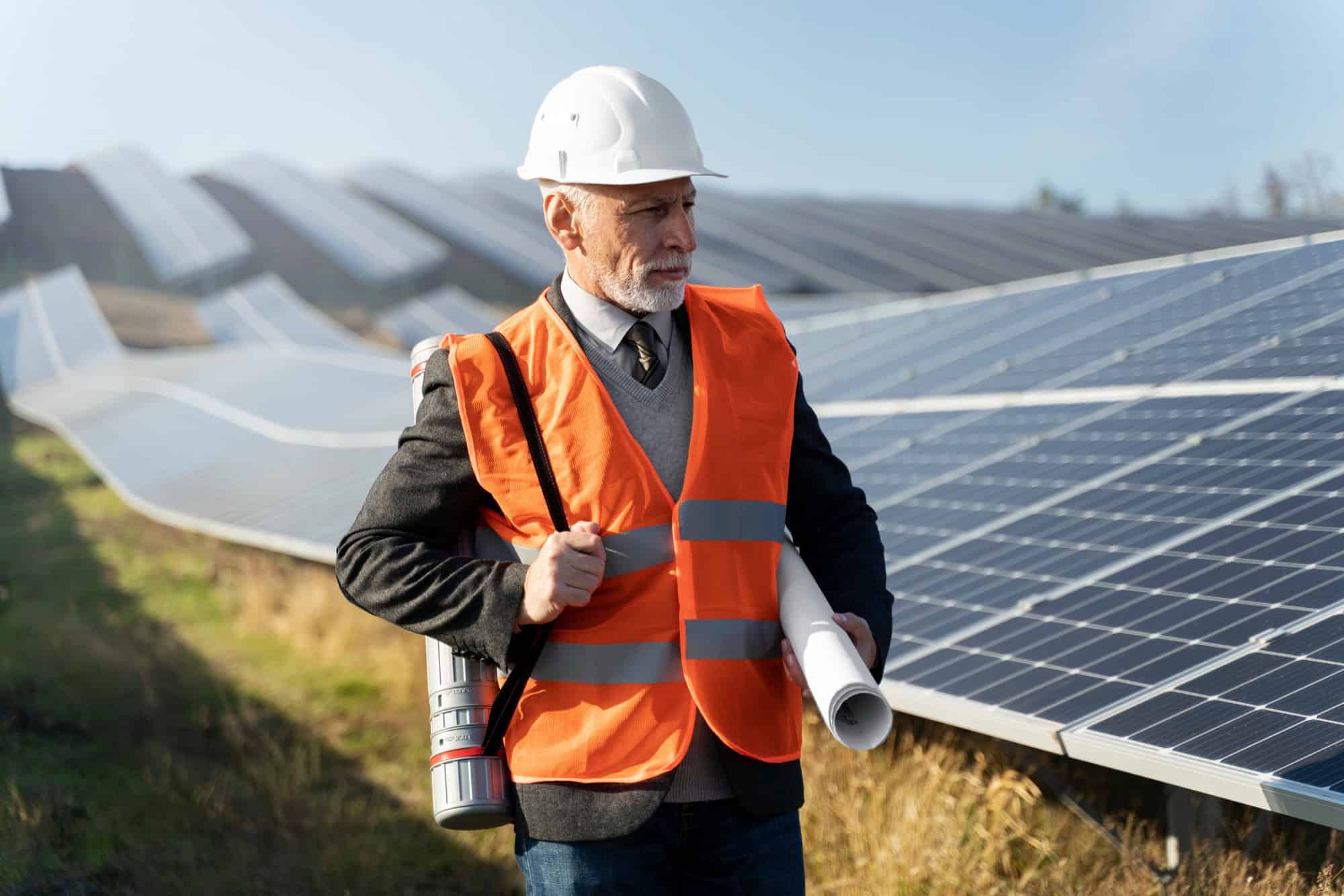 Ein Mann in einer orangen Warnweste steht vor einer PV-Anlage auf einer Wiese.